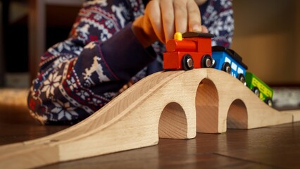 Closeup of boy in pajamas lying on floor and playing with toy wooden train and railroad.