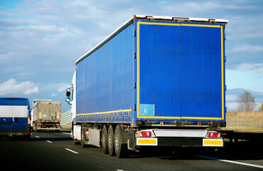 Modern blue semi-trailer trucks on the highway driving in the right lane. Commercial vehicle for shipping and post delivery. Shipping of the goods on land door-to-door