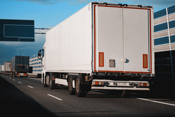 Modern white semi-trailer trucks on the highway driving in the right lane. Commercial vehicle for shipping and post delivery. Shipping of the goods on land door-to-door