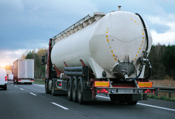 Petrol cargo truck driving on highway hauling oil products. Fuel delivery transportation. Aviation fuel transportation. Compressed gas carrier truck rear view on a highway. Dairy products carrier - obrazy, fototapety, plakaty
