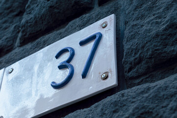 Number 37 building retro style white ceramic number plate with blue numbers, on the stone bricks background.