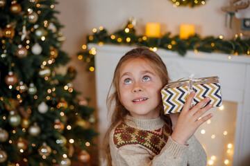 Adorable little girl of 5 years old with long curly hair and blue eyes opens gift boxes near the...