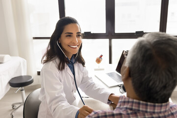Positive beautiful young practitioner woman examining senior patient man, applying stethoscope to...