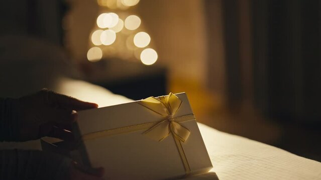 White Female Hands Opening White Box With Yellow Bow in Dimly Lit Room