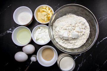 ingredients for baking on black marble. flour, butter, cream, sugar, salt, eggs, dry yeast, milk, vegetable oil