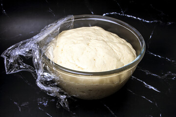 yeast dough in a transparent plate on a black marble background