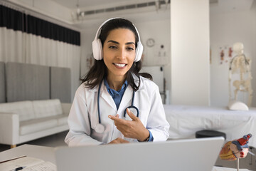 Positive young cardiologist doctor woman checking patients online, talking on video conference...