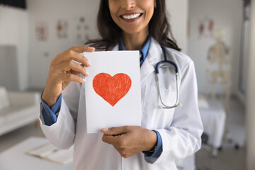 Cropped shot of young therapist doctor woman showing paper greeting card with drawn red heart at camera. Cardiologist promoting heart disease diagnosing, early medical examination - Powered by Adobe