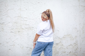 A beautiful plus size woman dressed  jeans, white t-shirt and  fashion  accessories. Latin american girl walking against white wall on the city street . Outdoor portrait of a elegant woman