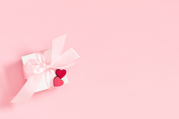 Valentine's Day background. Cute confetti hearts, gift box with bow on isolated pastel pink...