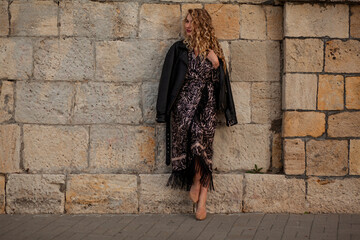Beautiful  woman walking in the street of the city. Blond with curly hair fashion model wears...