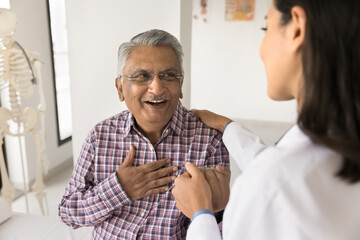 Young doctor woman calming senior Indian patient, holding mans hand, touching shoulder with comfort, support, compassion, telling good news about health, heart work - obrazy, fototapety, plakaty