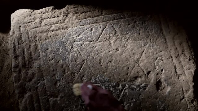 Top view hand of an archaeologist uses a brush to remove a layer of dirt and dust from an image of a six-pointed star of David on an ancient stone slab. historical discovery symbol of Israel