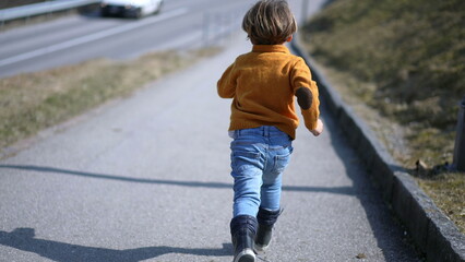 Back of excited small boy sprinting outside during autumn day, Child wearing yellow pullover,...