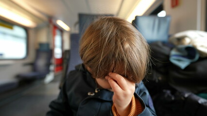 Child rubbing eye with hand while traveling by train. Small boy scratching face taking care of itch