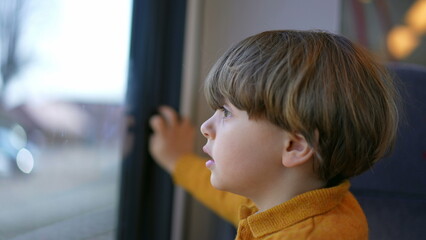 Close-up child face staring at view from train window with curious expression. One small caucasian...