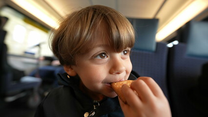 Close-up face of happy child eating butter biscuit while in travel commute, small boy snacking...