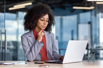 Serious focused and concentrated woman at workplace, thinking businesswoman looking at laptop screen, working inside office at workplace, solving financial technical tasks - obrazy, fototapety, plakaty