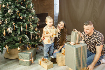 a young family with a small child unwraps gifts near the Christmas tree. family in the living room...