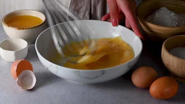 Whisking egg in bowl with a metal wire whisk. Cooking process, baking, breakfast.