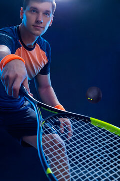 Squash player on a squash court with racket. Man athlete with racket on court with neon colors. Sport concept. Download a high quality photo for the design of a sports app or betting site.