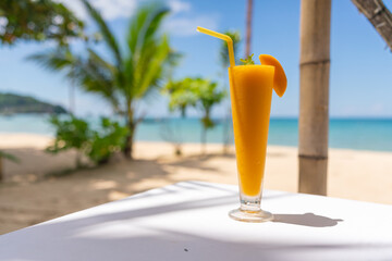 Photo of a glass of ice blended fruit punch juice against the backdrop of a beautiful beach with coconut tree.