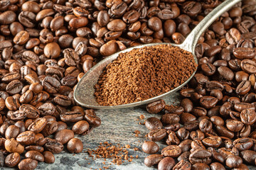 A spoon filled with ground coffee lies among a pile of coffee beans