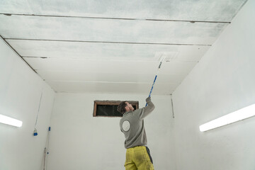 Diligent Worker in Grey Jumper and Yellow Trousers Adds Final Strokes to White Garage Paint Job.