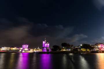 Fototapeta na wymiar Panoramic view of the La Rochelle old harbor with its famous towers. night shot with pink lights for pink october. Pink October is breast cancer awareness month
