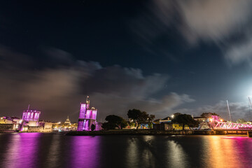 Fototapeta na wymiar Panoramic view of the La Rochelle old harbor with its famous towers. night shot with pink lights for pink october. Pink October is breast cancer awareness month