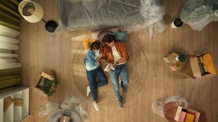 Top view of apartment living room. Man and woman laying on the floor in new apartment looking at...