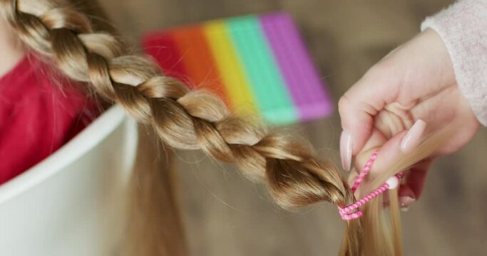 A beautiful golden braid of a child, fixing the end of the braid with a children's elastic band.