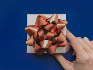 Woman hand holding a gift with gold ribbon bow on blue background