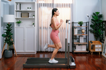 Fototapeta na wymiar Full length side view of energetic and strong athletic asian woman running running machine at home. Pursuit of fit physique and commitment to healthy lifestyle with home workout and training. Vigorous