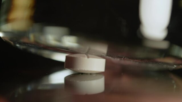Pills crushing Into powder with kitchen glass in slow motion, extreme macro close up. Addicted people using for snorting. The medicine is crushed on the table.