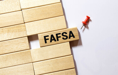 Businessman hand holding wooden cube block with FAFSA business word on table background.