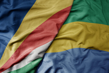 big waving national colorful flag of seychelles and national flag of gabon .