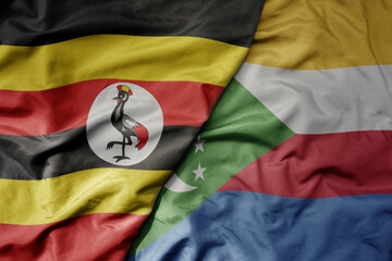big waving national colorful flag of uganda and national flag of comoros .