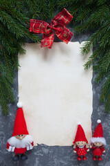 Christmas background with fir branches, gnomes, red ribbon bow and old paper for text on gray plaster. Copy space, top view.