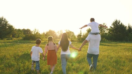 Father carries son on shoulders walking with family across field in summer