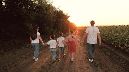 Large family with children walks holding hands along rural road at sunset