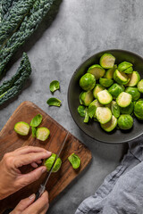 top view of a person cutting Brussels sprouts on a wooden cutting board, grey background, space for text
