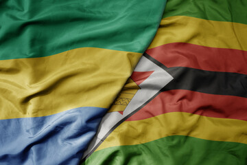 big waving national colorful flag of zimbabwe and national flag of gabon .