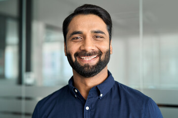 Happy bearded Indian business man leader looking at camera standing in office. Professional smiling...