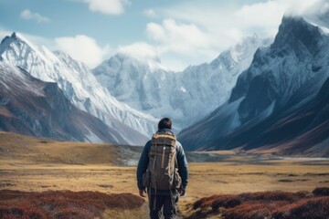 A lone traveler with a backpack looking out over a vast mountainous landscape with a mix of snow peaks and autumn vegetation