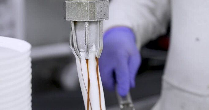 Food industry. Ice cream production process. Closeup view of creamy white ice cream with caramel, coming our from a pipe manipulated by a factory worker. 