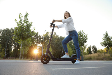 Happy woman riding modern electric kick scooter in park, low angle view