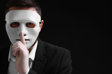 Man in mask and gloves showing hush gesture against black background. Space for text