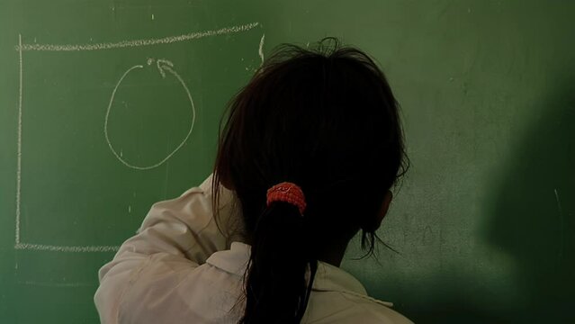 School Girl Writing on Green Chalkboard During a Class in a Public School in Argentina. Close Up.