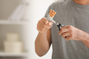 Stop smoking concept. Man cutting cigarettes on blurred background, closeup. Space for text